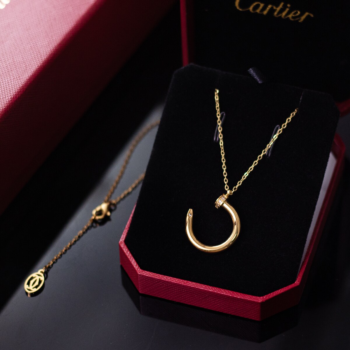 Gold tone nail motif pendant necklace presented on a dark display