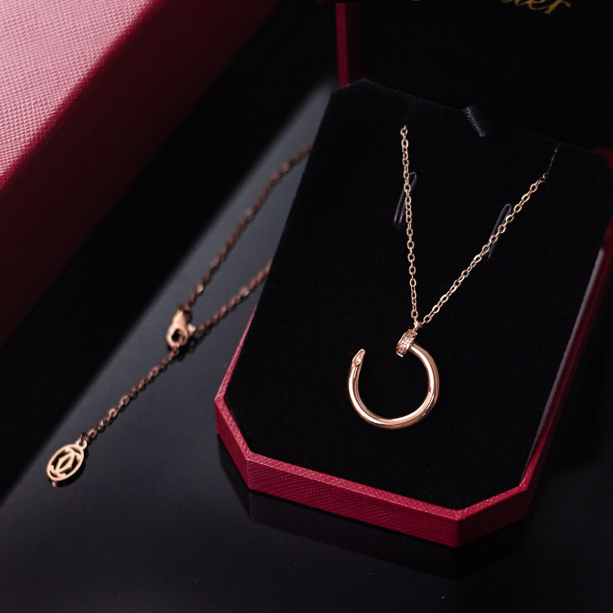 Rose gold tone nail motif pendant necklace presented on a dark display