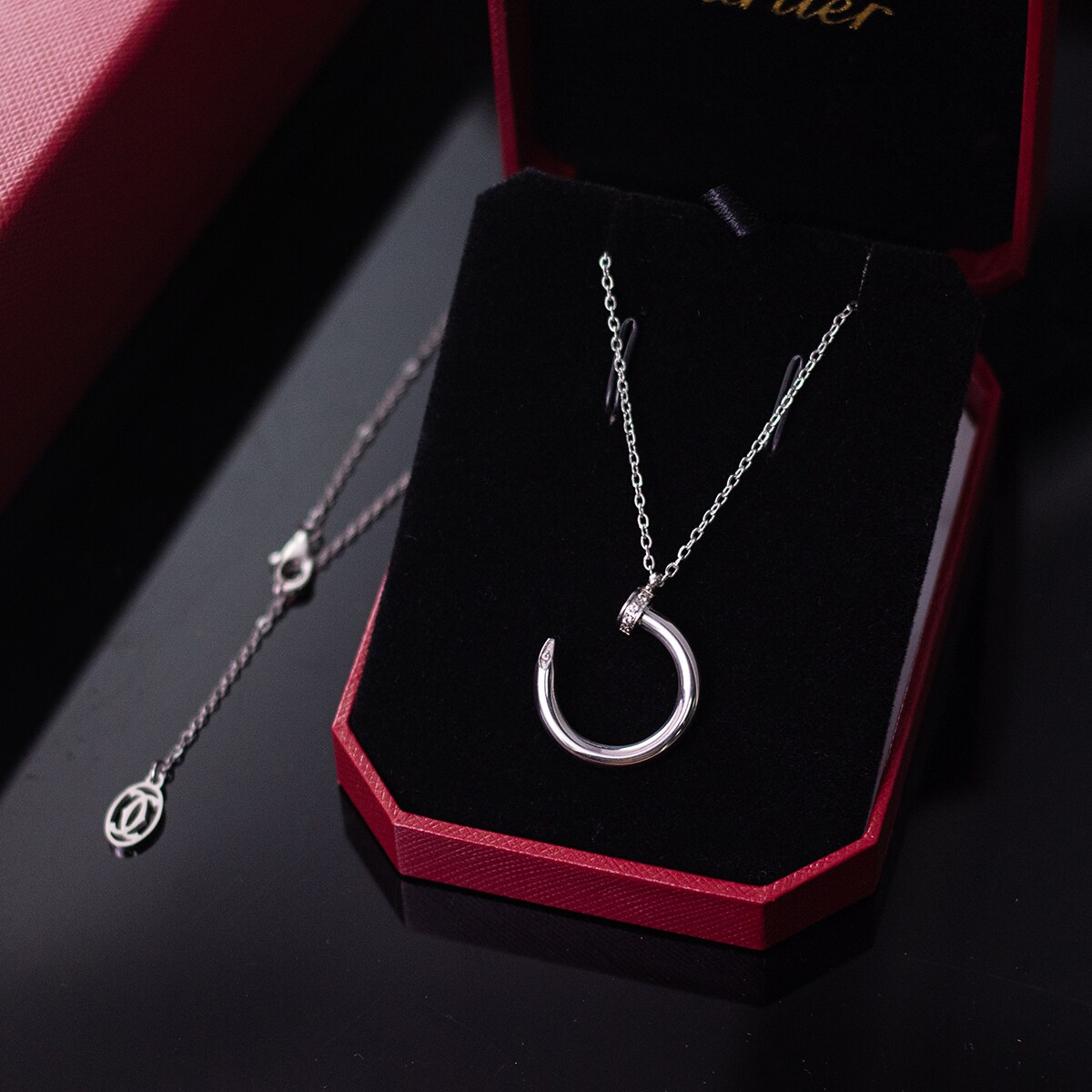 Silver tone nail motif pendant necklace presented on a dark display